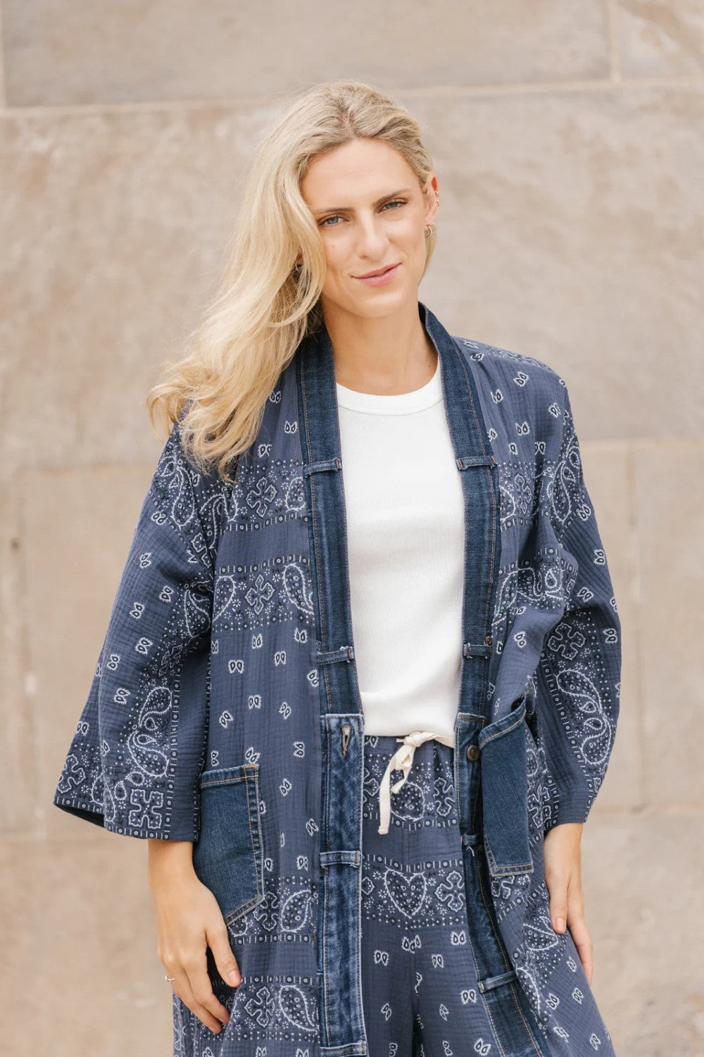 Woman wearing a blue patterned kimono-style garment against a stone wall.