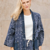 Woman wearing a blue patterned kimono-style garment against a stone wall.