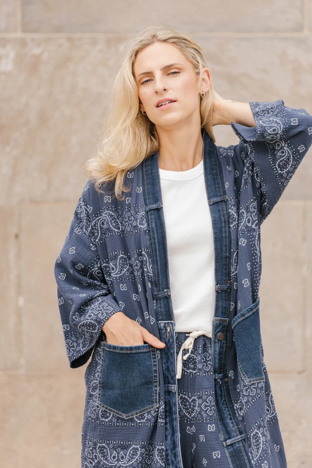 Woman wearing a blue patterned kimono-style garment against a beige wall.