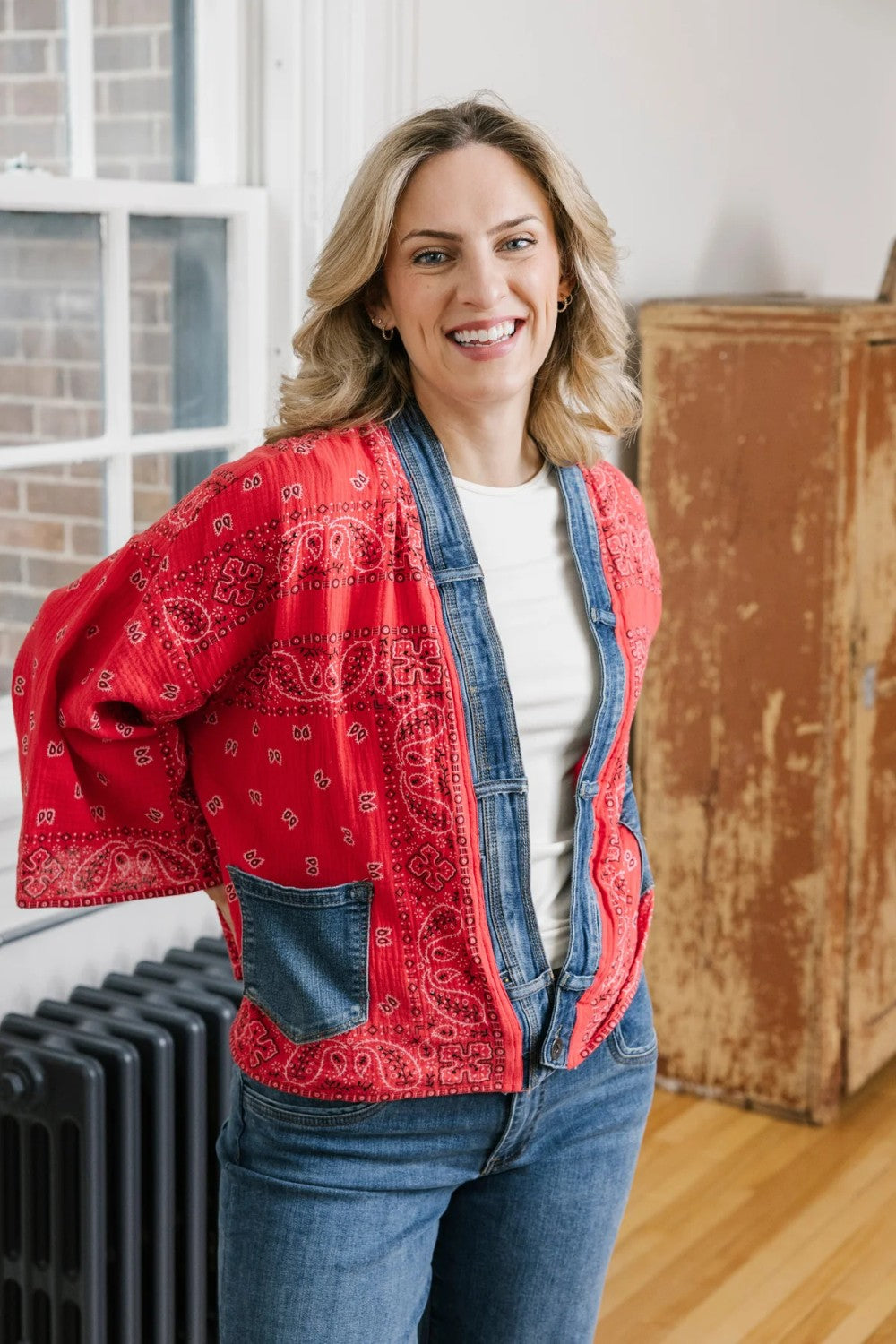 Woman wearing a red patterned jacket over a denim outfit indoors.