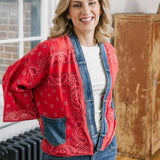 Woman wearing a red patterned jacket over a denim outfit indoors.