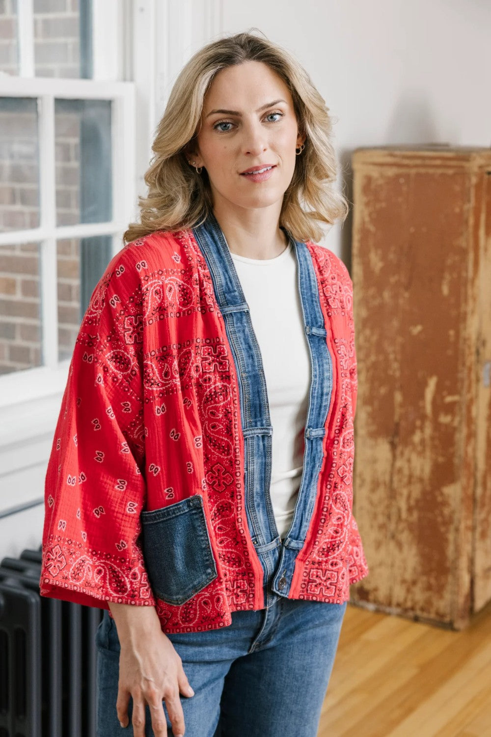 Woman wearing a red patterned jacket over a denim jacket indoors.