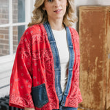 Woman wearing a red patterned jacket over a denim jacket indoors.