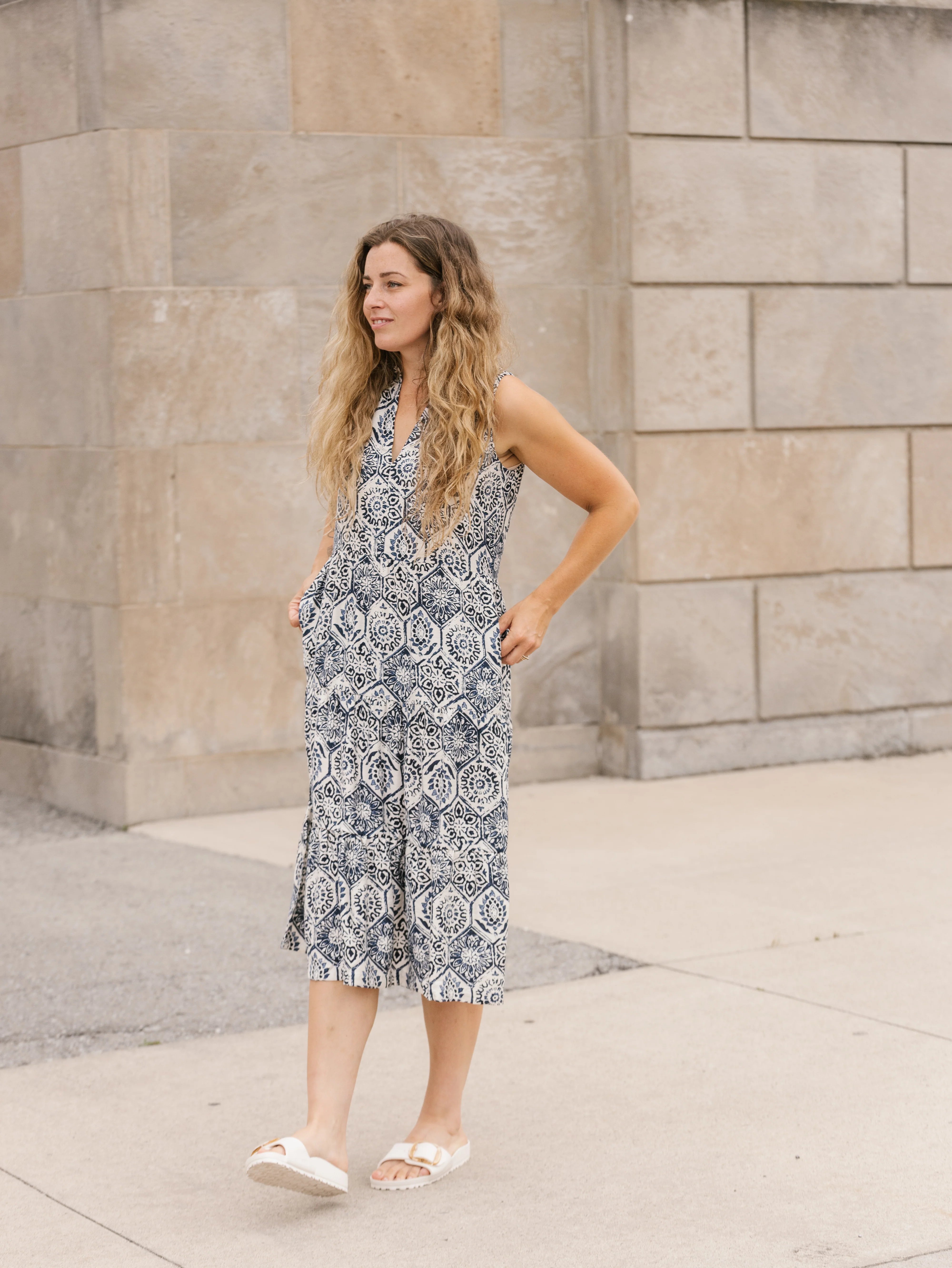 Woman wearing a patterned dress standing against a stone wall.