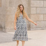Woman in a patterned dress standing against a stone wall.