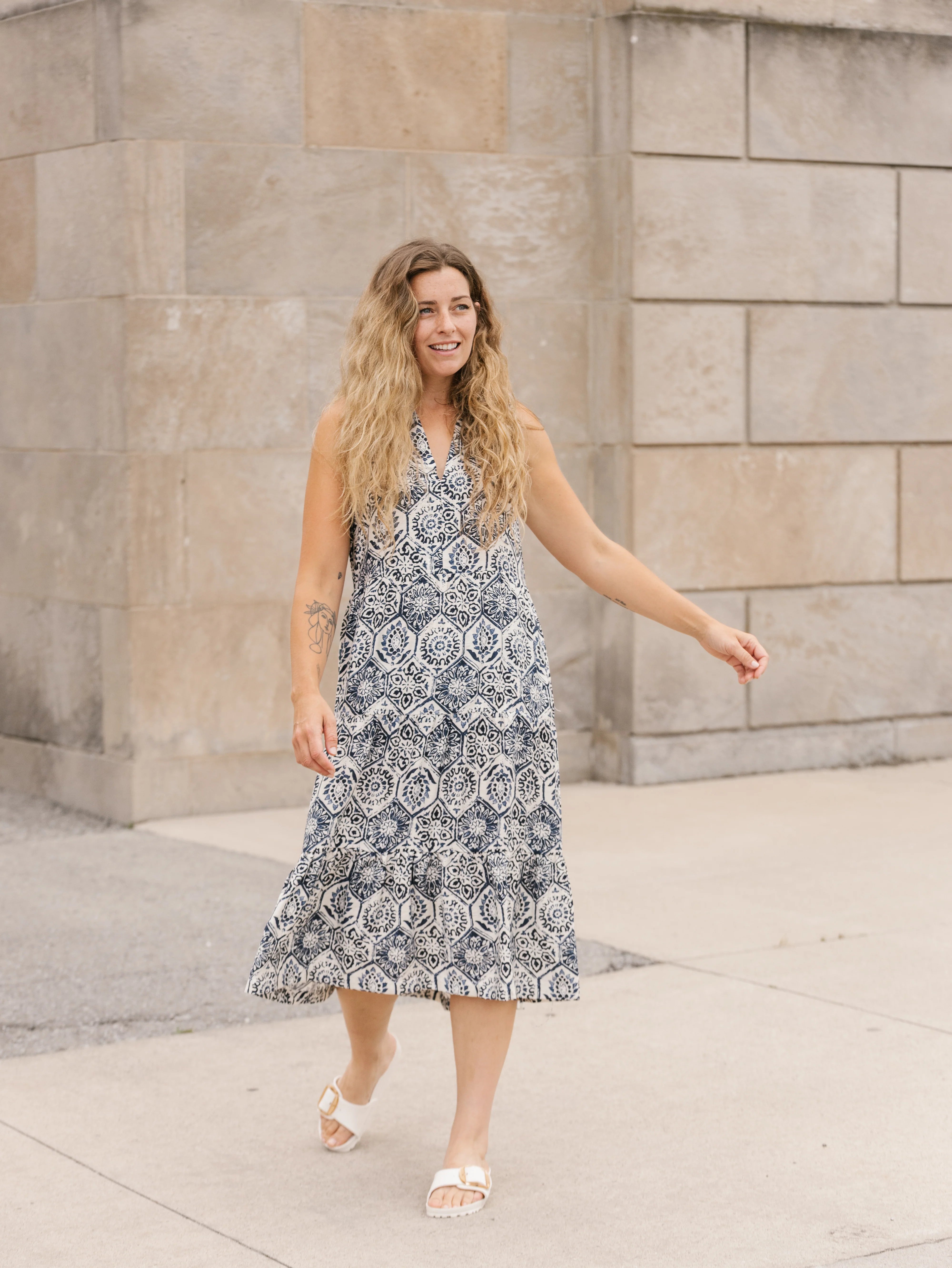Woman in a patterned dress standing against a stone wall.