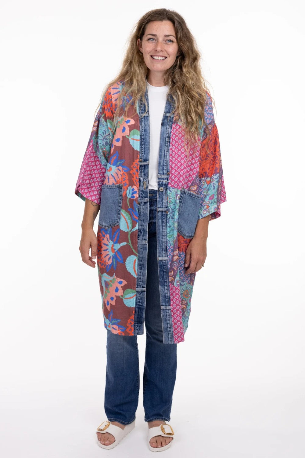 Woman wearing a colorful patchwork kimono over a white shirt and jeans on a white background