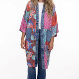 Woman wearing a colorful patchwork kimono over a white shirt and jeans on a white background