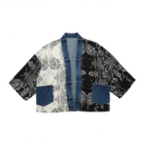 A cropped open-front jacket featuring a patchwork design with a white and black floral print, solid black floral print, and blue denim panels and trim, displayed flat against a white background.