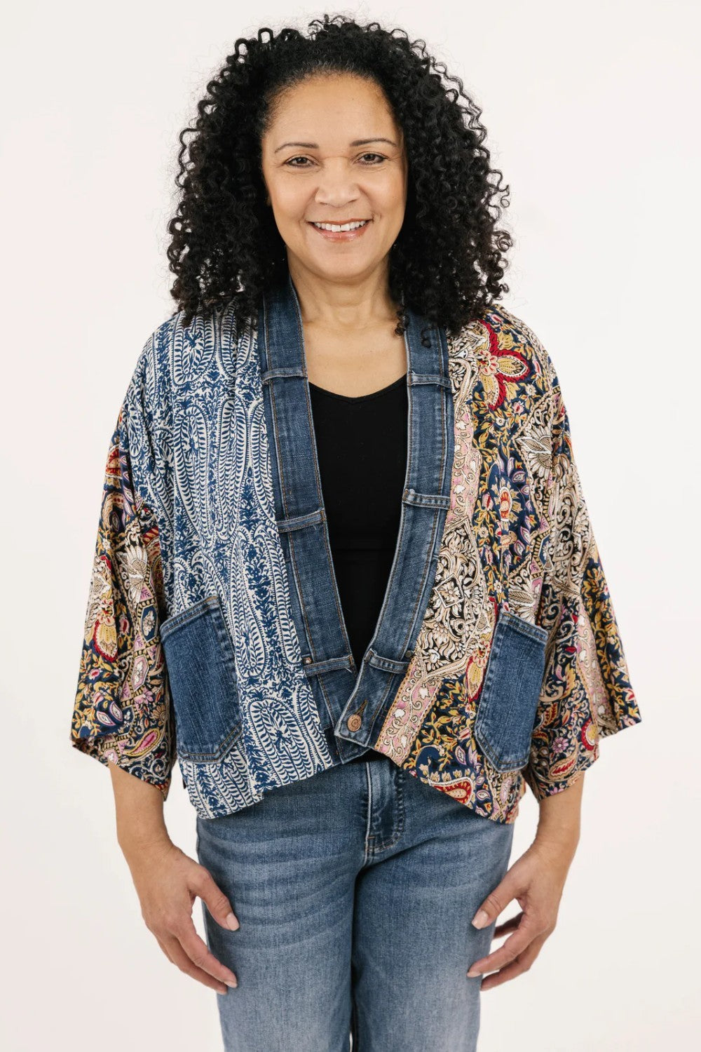 Woman wearing a colorful jacket over a black shirt and jeans on a white background