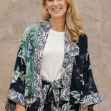 Woman wearing a palm print kimono-style outfit against a stone wall.