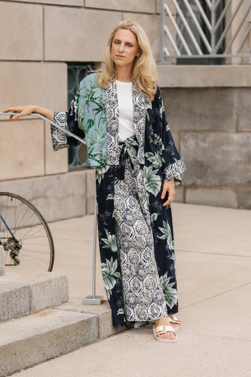 Woman wearing a palm print kimono-style outfit standing outdoors.