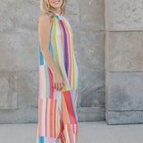 Woman wearing a colorful striped dress standing against a stone wall.