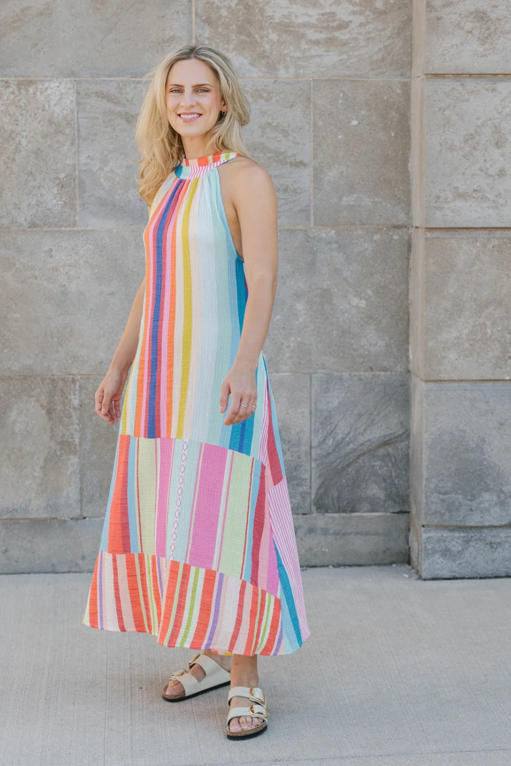 Woman wearing a colorful striped dress standing against a stone wall.