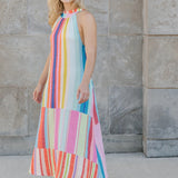Woman wearing a colorful striped dress standing against a stone wall.