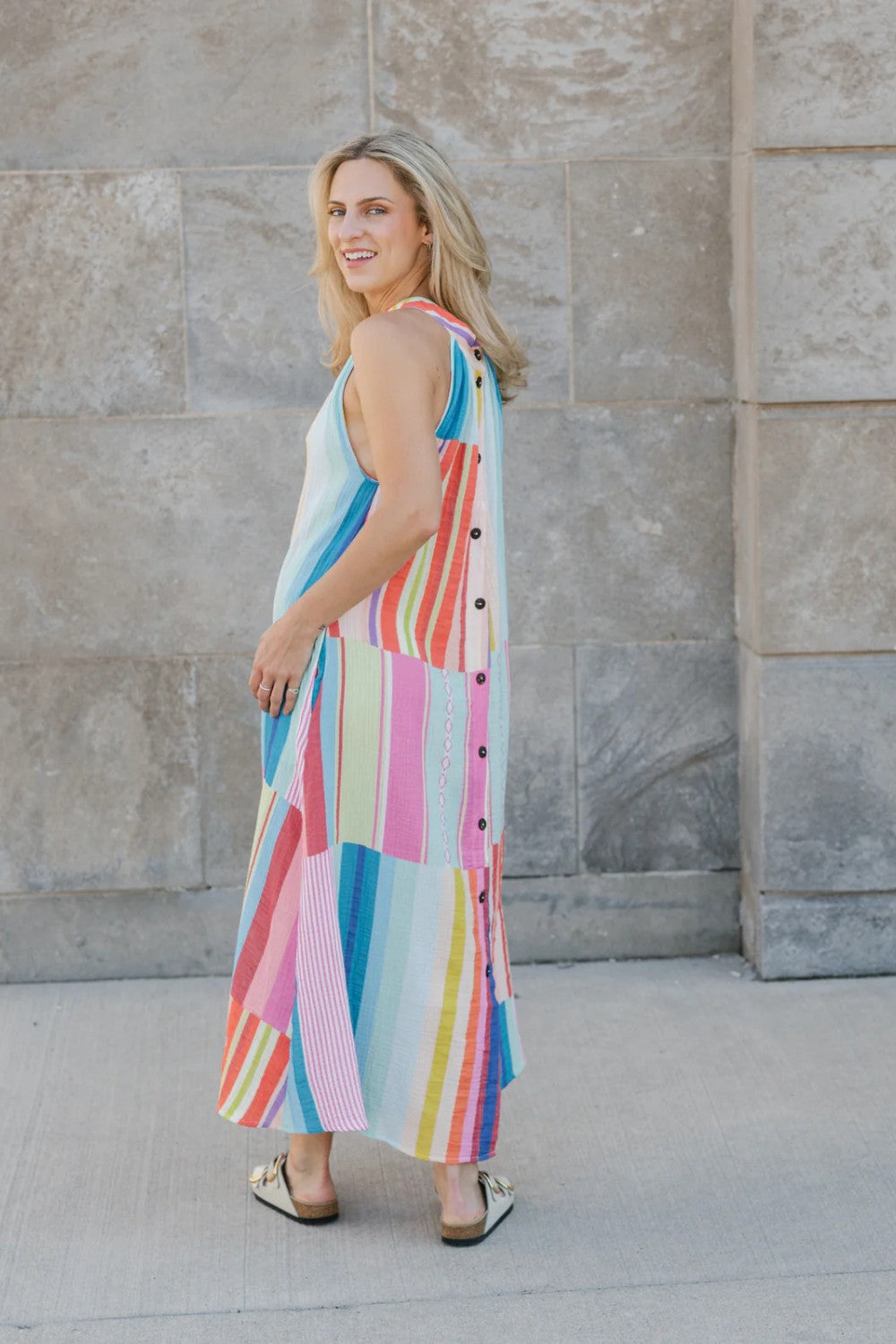 Woman wearing a colorful striped dress standing against a stone wall.