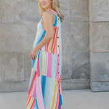 Woman wearing a colorful striped dress standing against a stone wall.