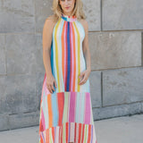 Woman wearing a colorful striped dress standing against a stone wall.