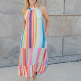 Woman wearing a colorful striped dress standing against a stone wall.