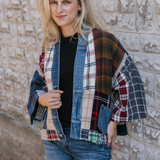 Woman standing in front of a stone wall wearing a black t-shirt and blue jeans with a mixed plaid fabric cardigan with denim trim and pockets.