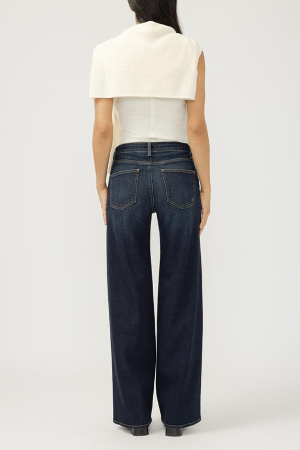 Person wearing dark blue jeans and a white top on a plain background