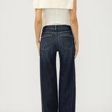 Person wearing dark blue jeans and a white top on a plain background