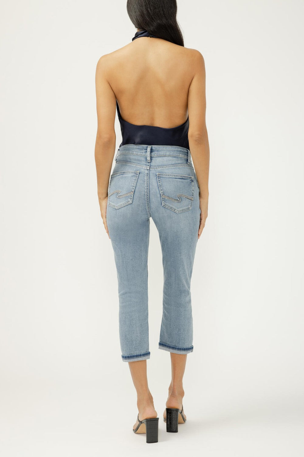 Woman wearing light blue jeans and a black top on a white background