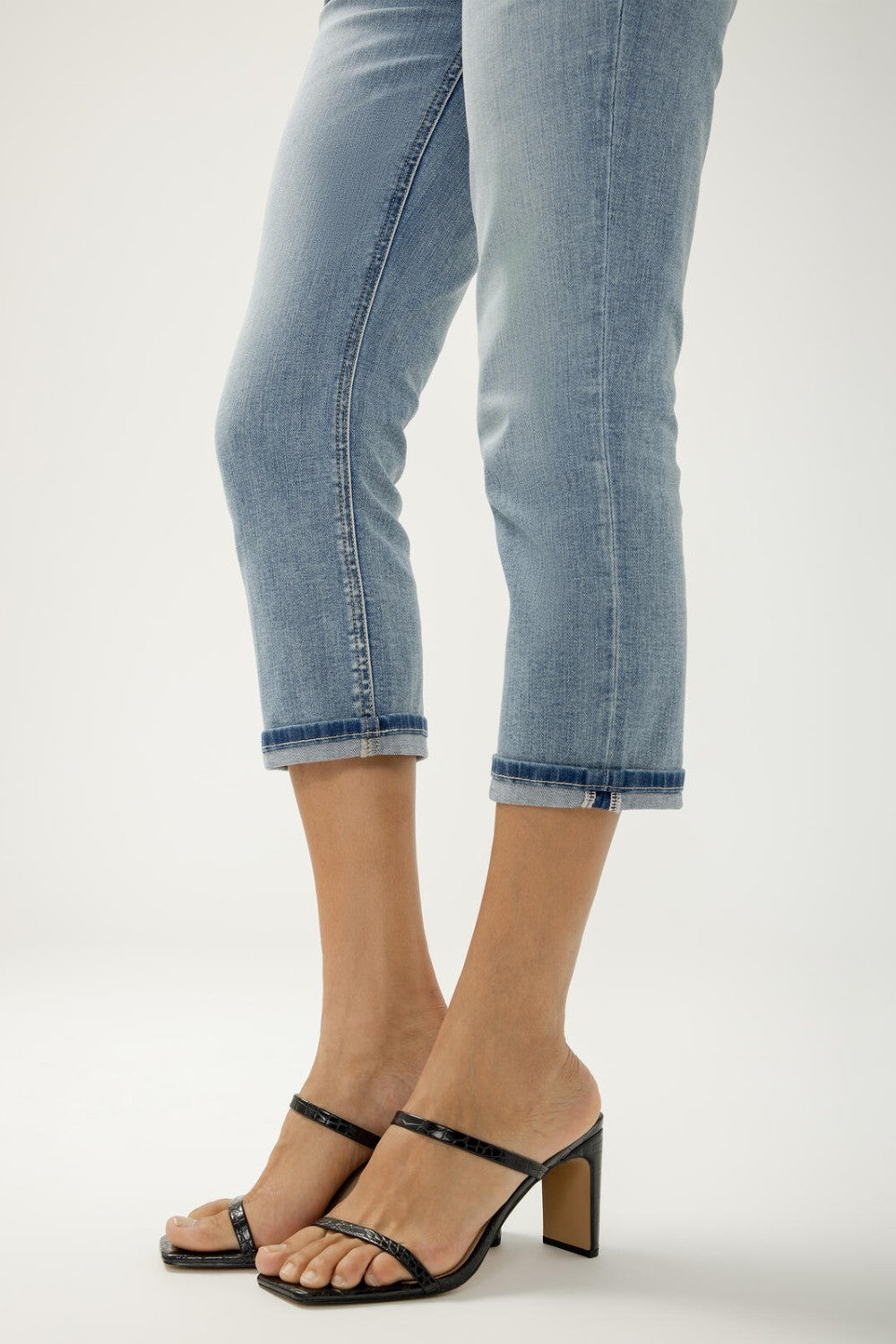 Person wearing light blue jeans and black heeled sandals on a white background