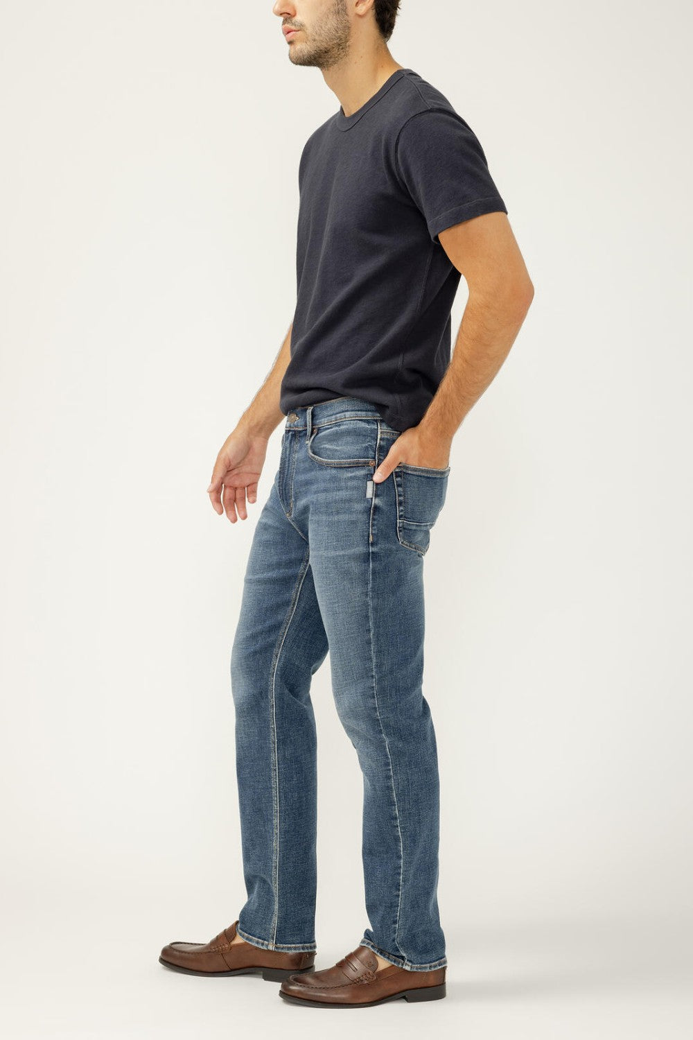 Man wearing a dark blue t-shirt and light blue jeans on a white background