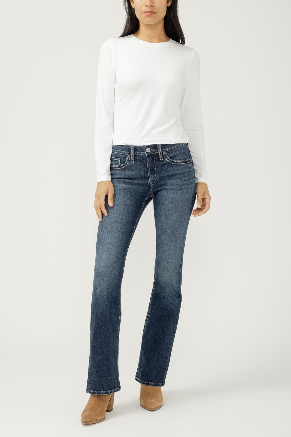 Woman wearing bootcut blue jeans with a white top on a light backdrop