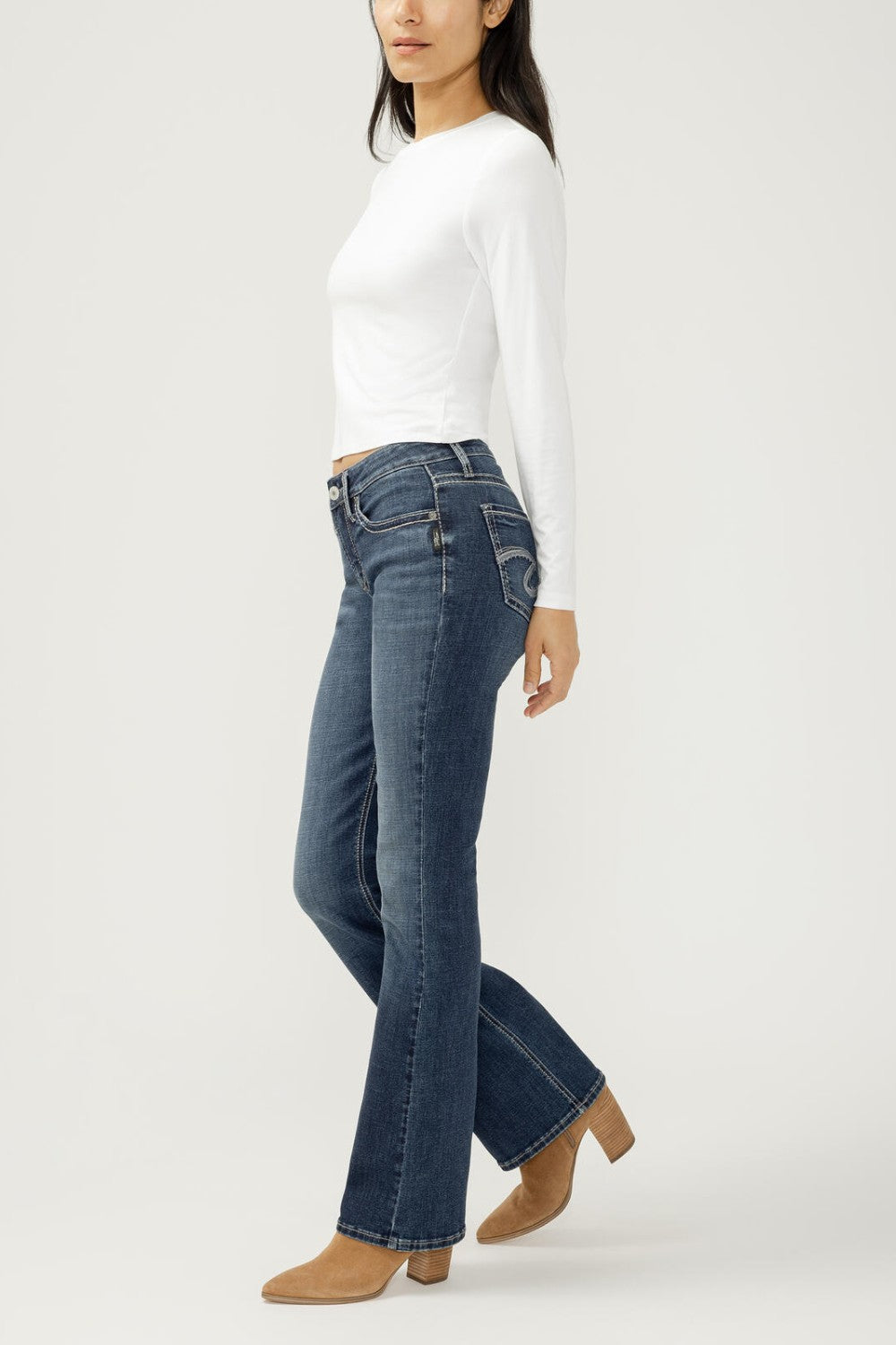 Woman wearing bootcut blue jeans with a white top on a light backdrop