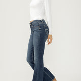 Woman wearing bootcut blue jeans with a white top on a light backdrop