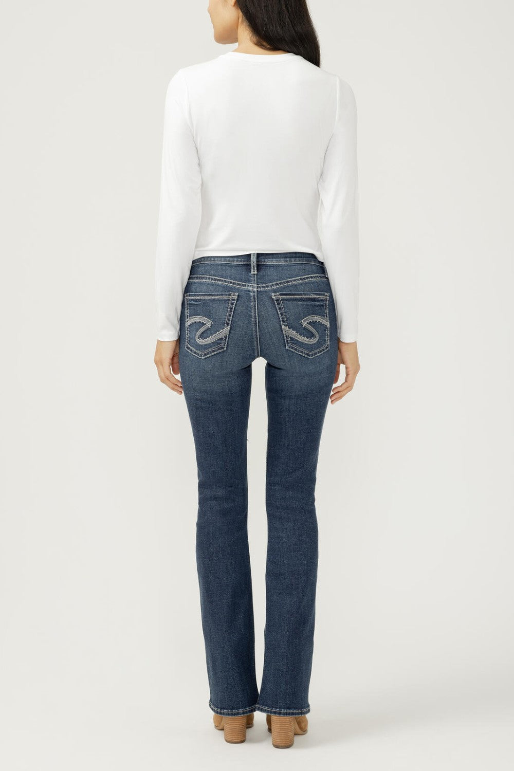 Woman wearing bootcut blue jeans with a white top on a light backdrop
