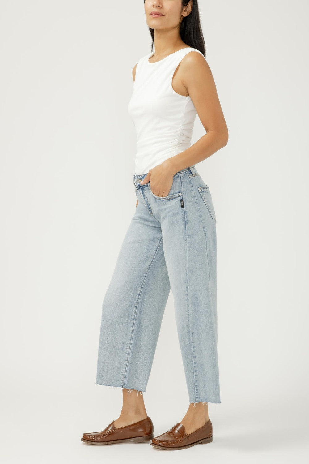 Woman wearing light blue jeans and a white top on a plain background