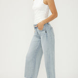 Woman wearing light blue jeans and a white top on a plain background