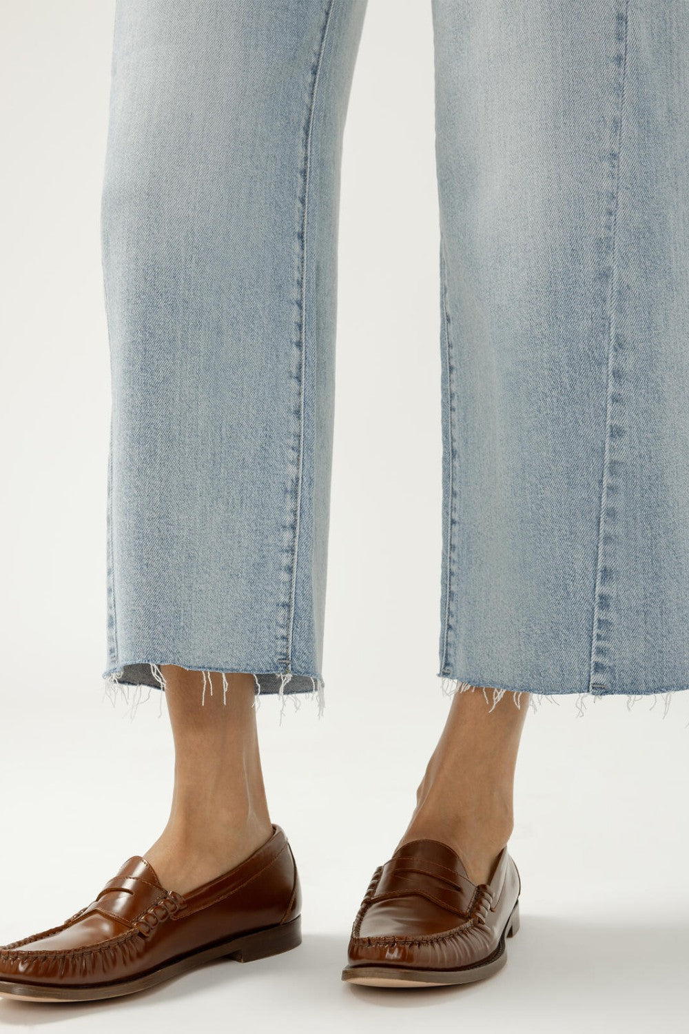 Person wearing light blue jeans and brown loafers on a white background
