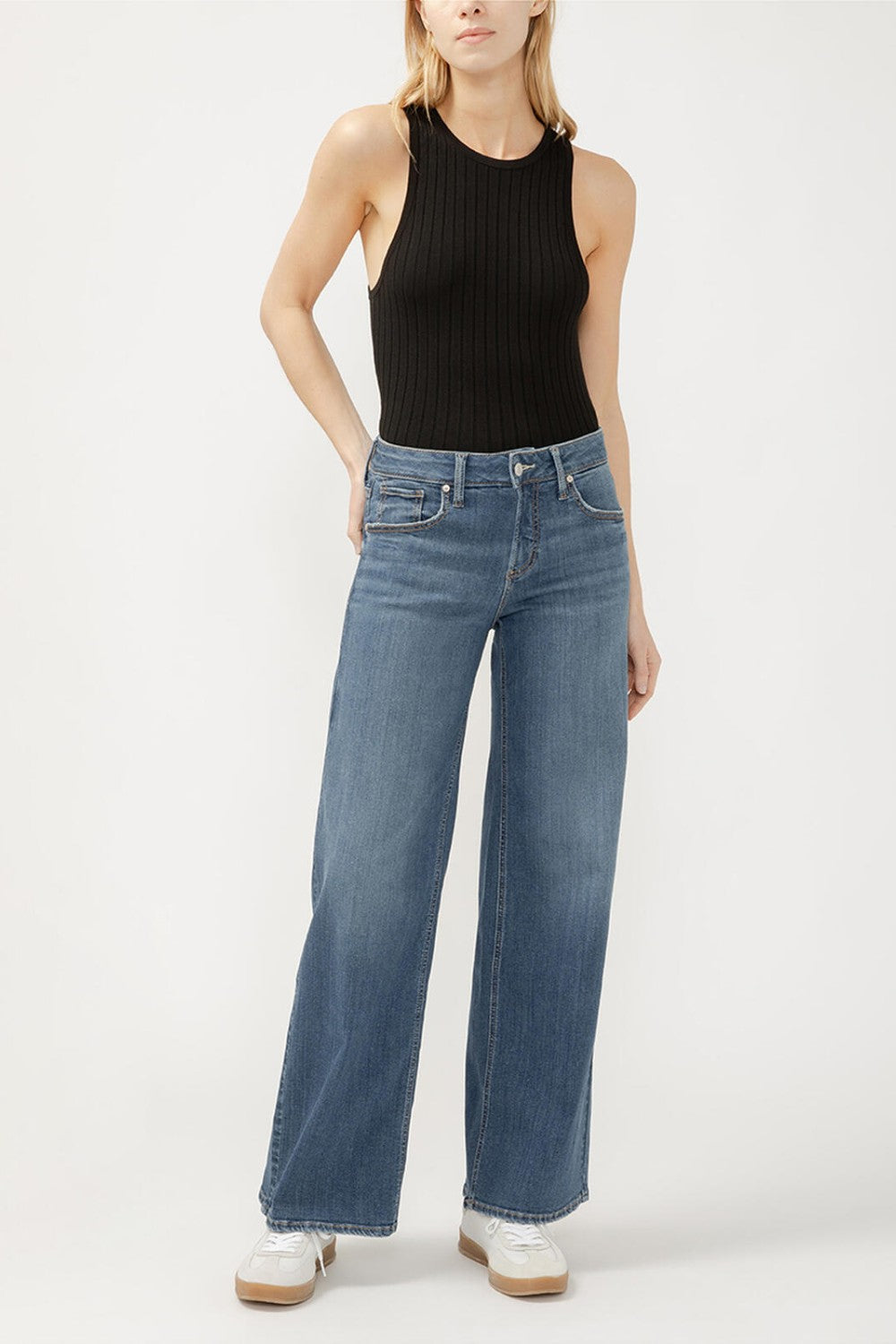 Person wearing a black sleeveless top and blue jeans on a white background