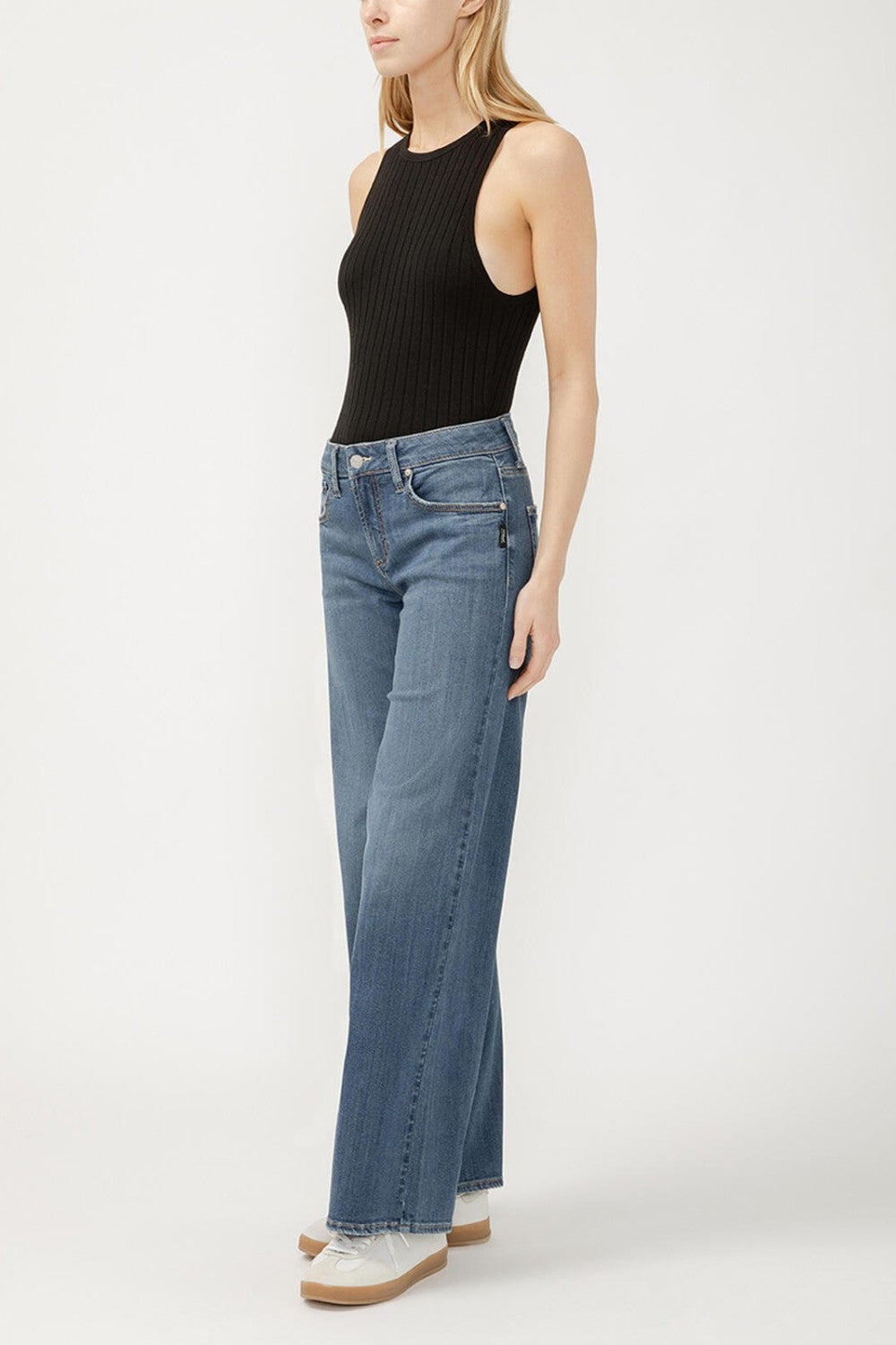 Person wearing a black sleeveless top and blue jeans on a white background