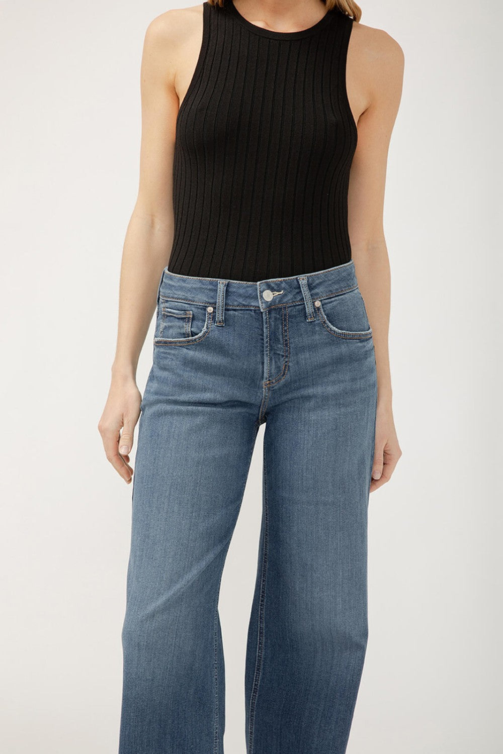 Person wearing a black ribbed tank top and blue jeans on a white background