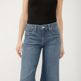 Person wearing a black ribbed tank top and blue jeans on a white background