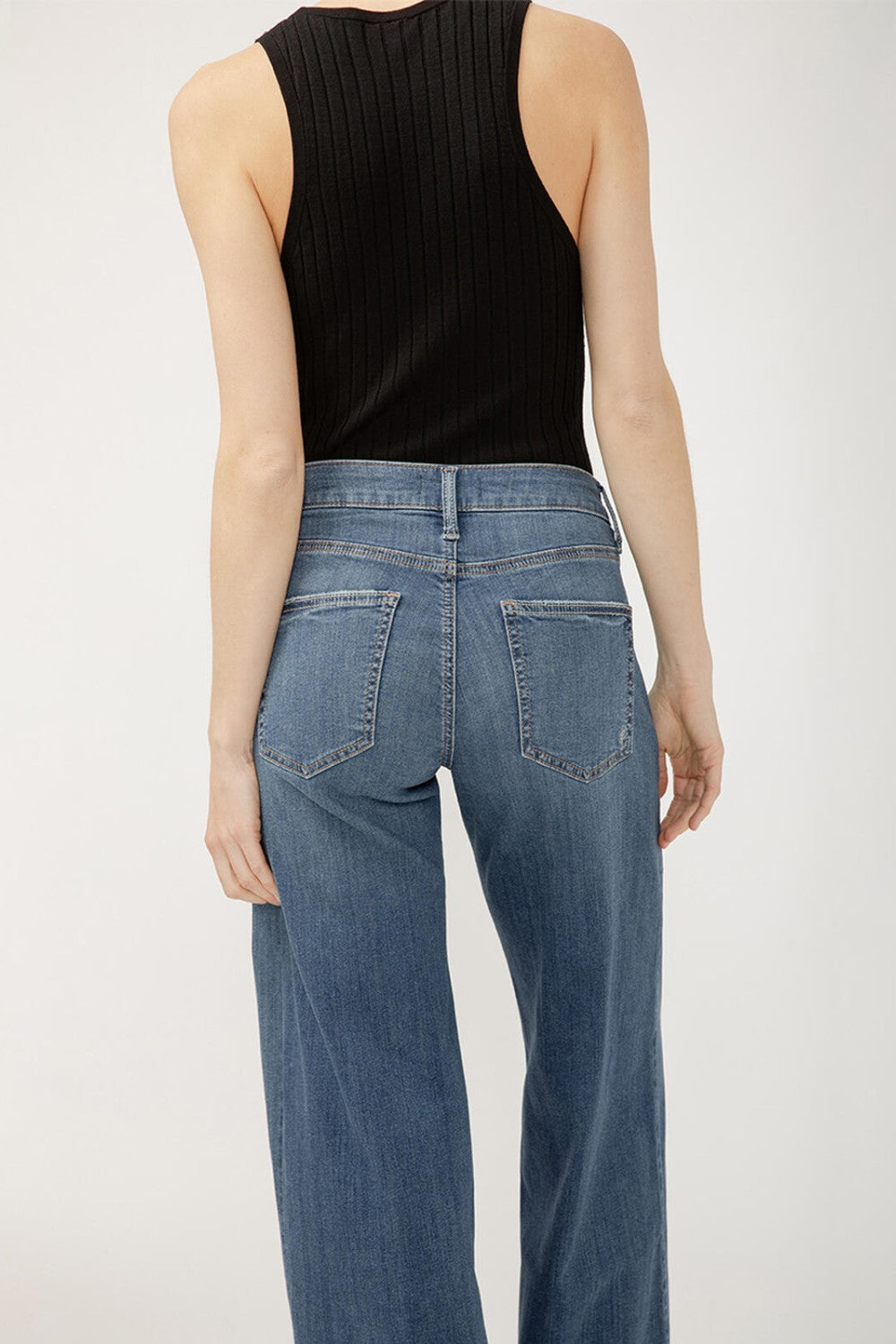 Person wearing blue jeans and a black sleeveless top on a white background