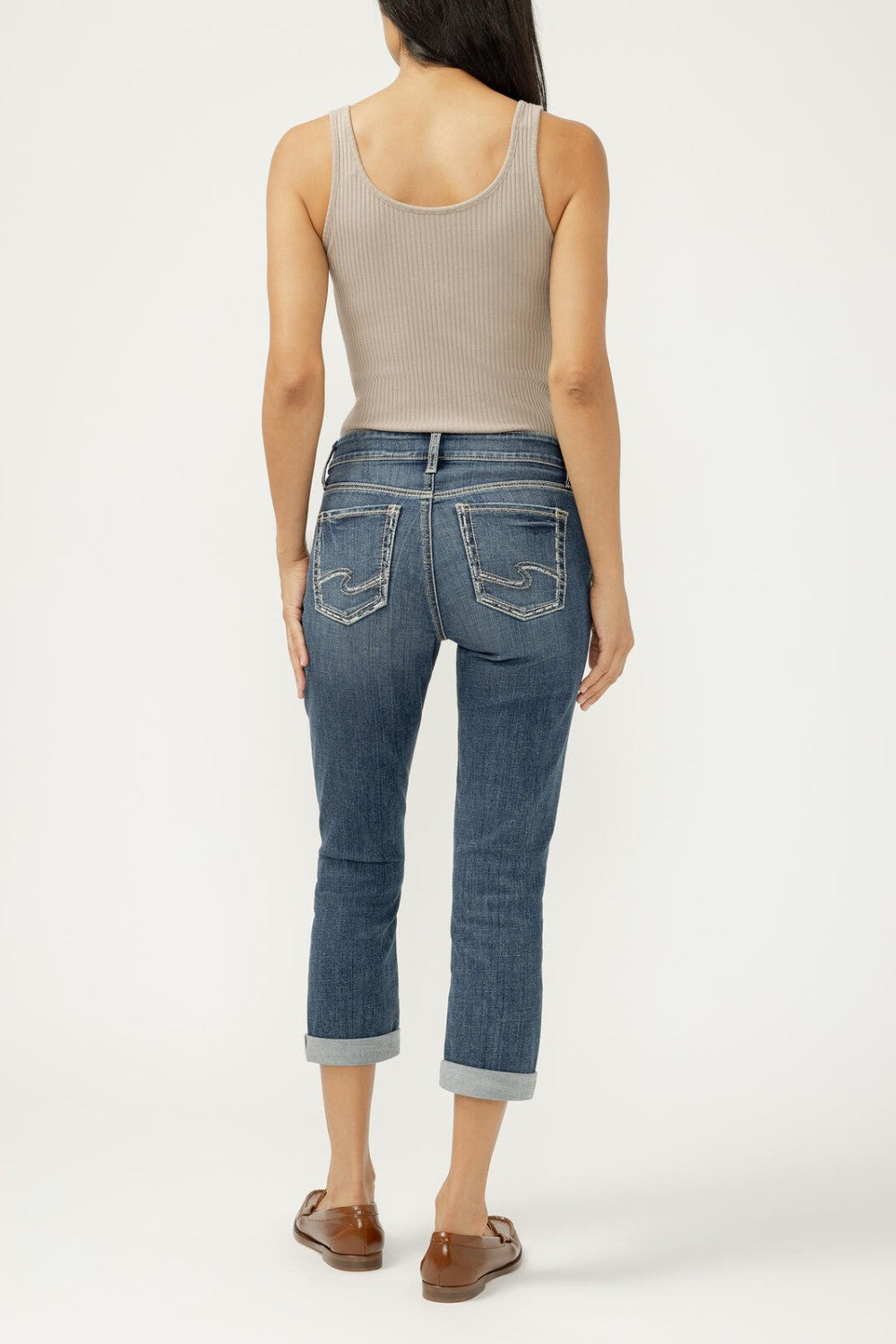 Person wearing a beige tank top and blue jeans on a white background