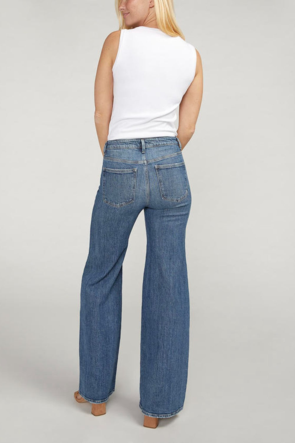 Person wearing blue jeans and a white top on a plain background