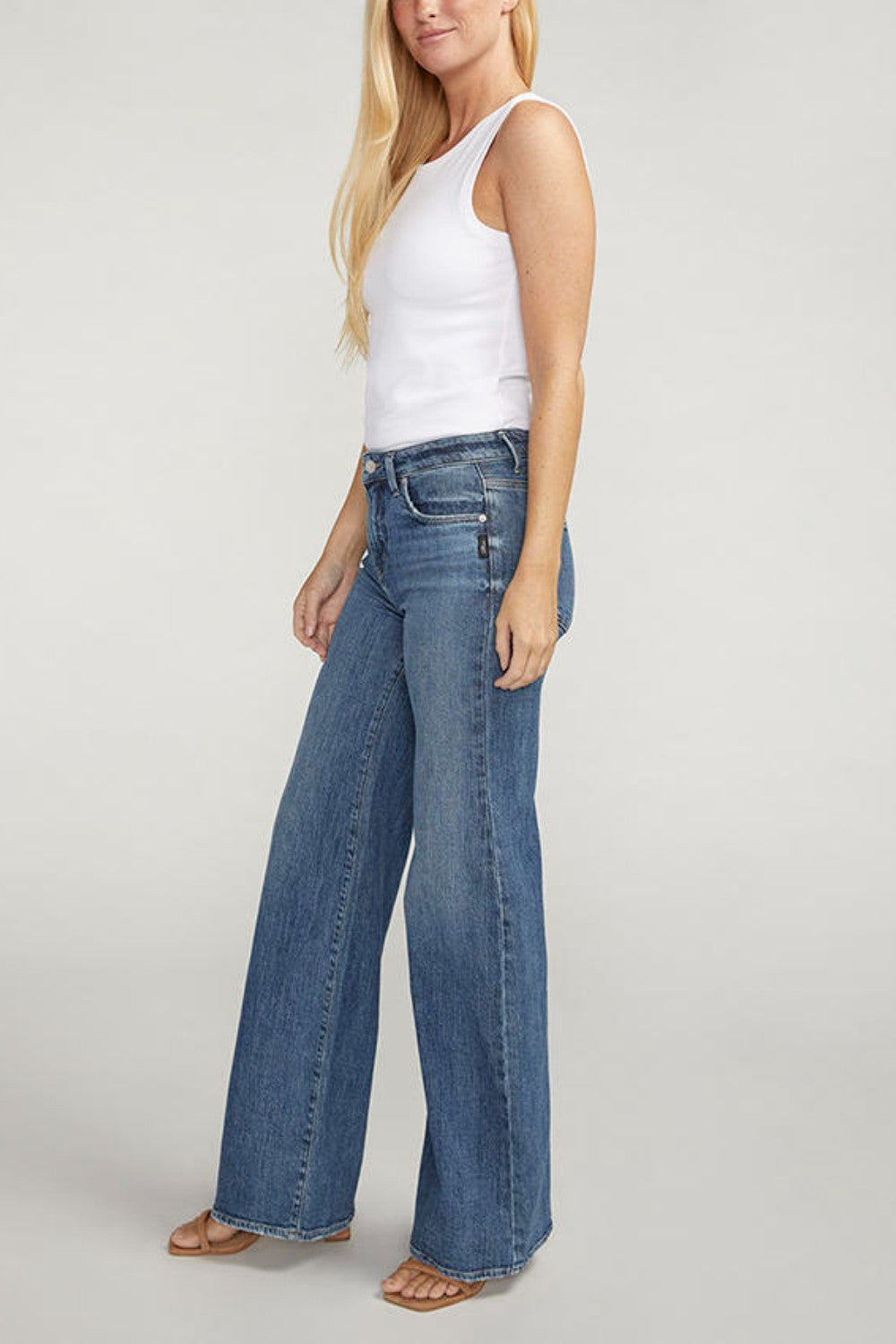 Woman wearing a white tank top and blue jeans on a plain background