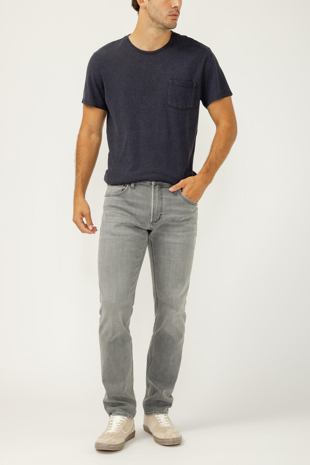 Man wearing a navy t-shirt and gray jeans on a white background