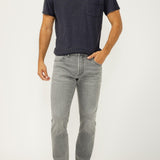 Man wearing a navy t-shirt and gray jeans on a white background