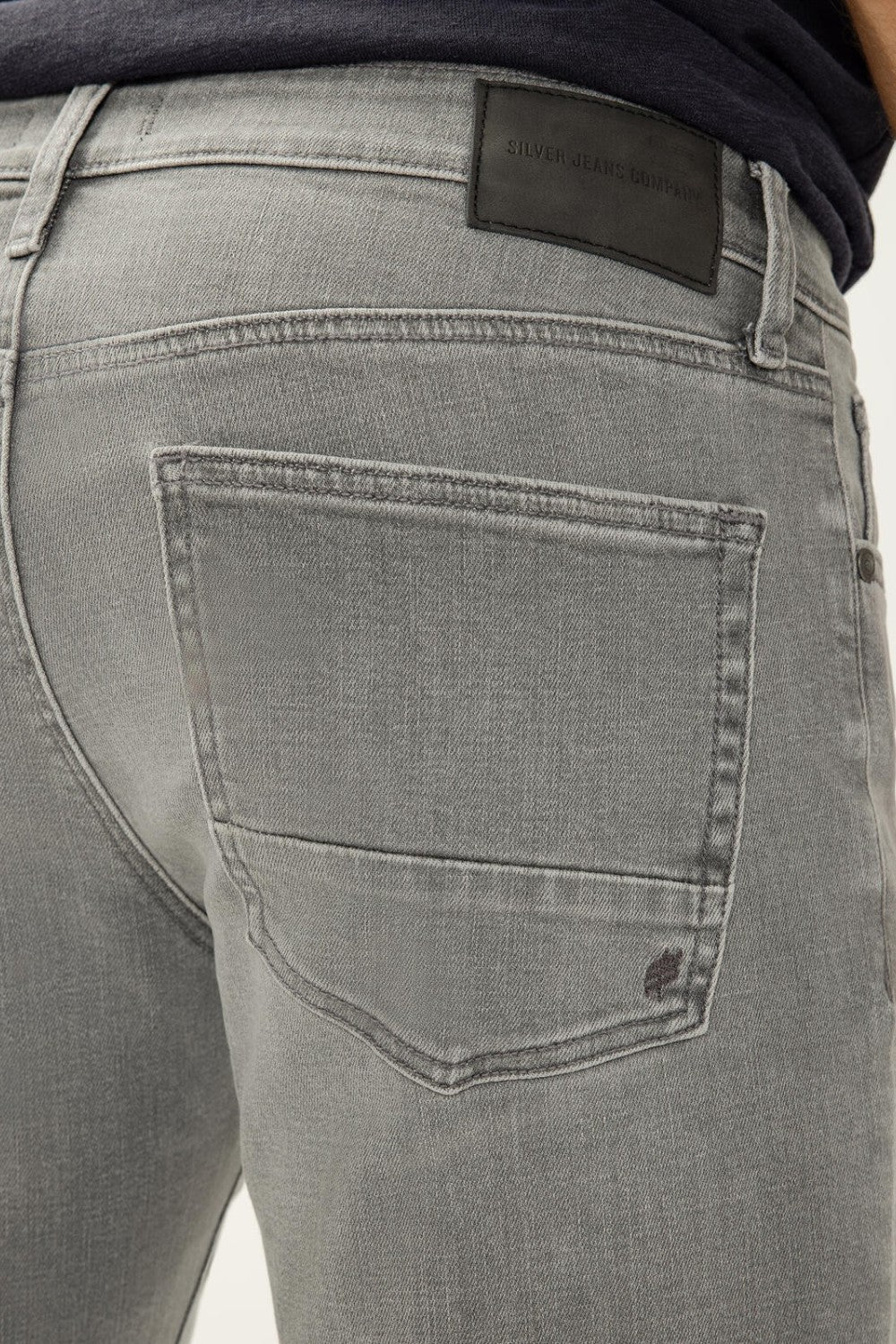 Gray jeans with a brand label on the back pocket against a neutral background