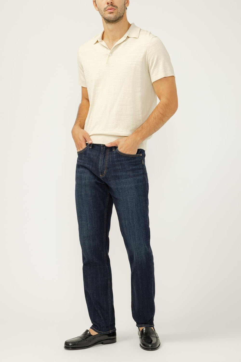 Man wearing a white polo shirt and dark blue jeans on a white background