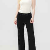 Woman wearing black jeans with a sleeveless white top and dark shoes against a light backdrop.