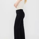 Woman wearing black jeans with a sleeveless white top and dark shoes against a light backdrop.